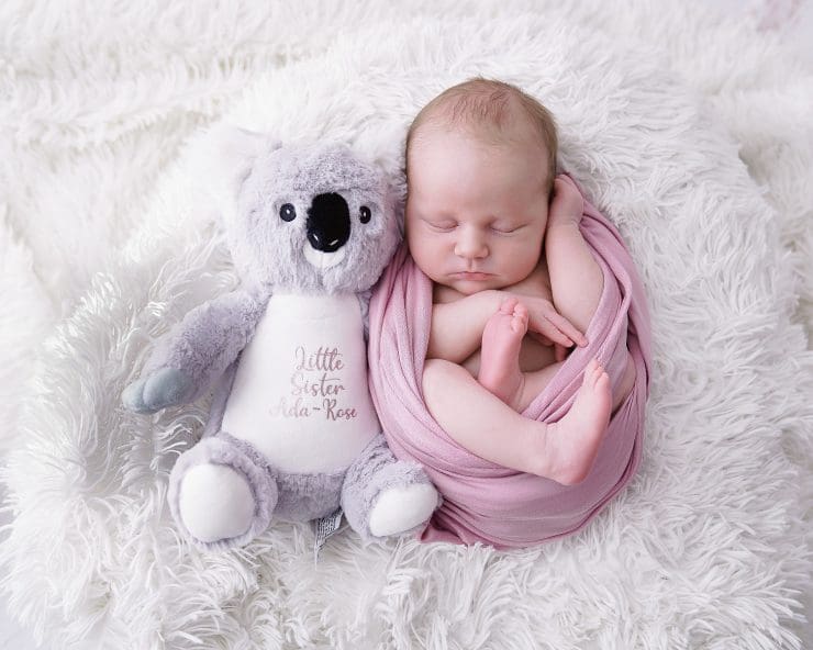 newborn baby photo where the baby is curled up tightly in a pink wrap with her legs hanging out while she sleep next to her cudly toy