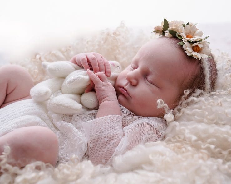 newborn baby girl laying on cream curls holding a toy rabit