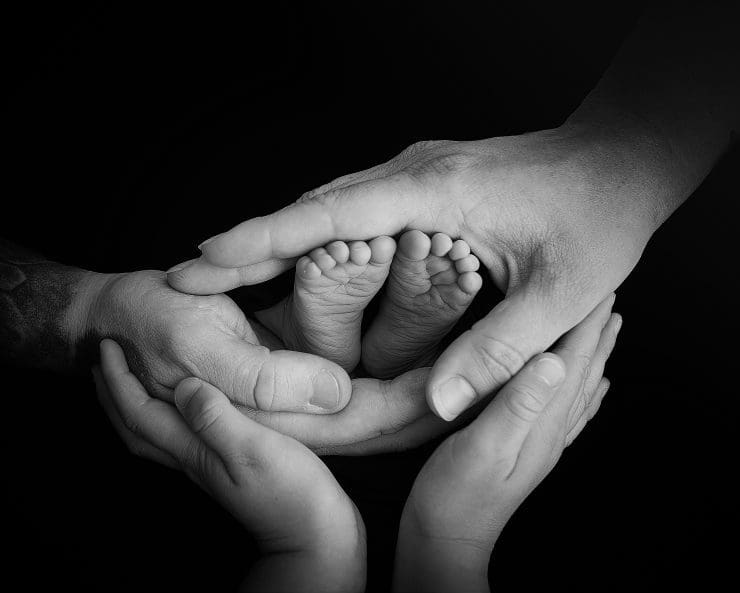 newborn baby toes surounded by her parents and big sisters hands, the photo is black and white