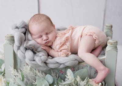 newborn baby girl fast asleep on a small green bed, with grey knitted blanket