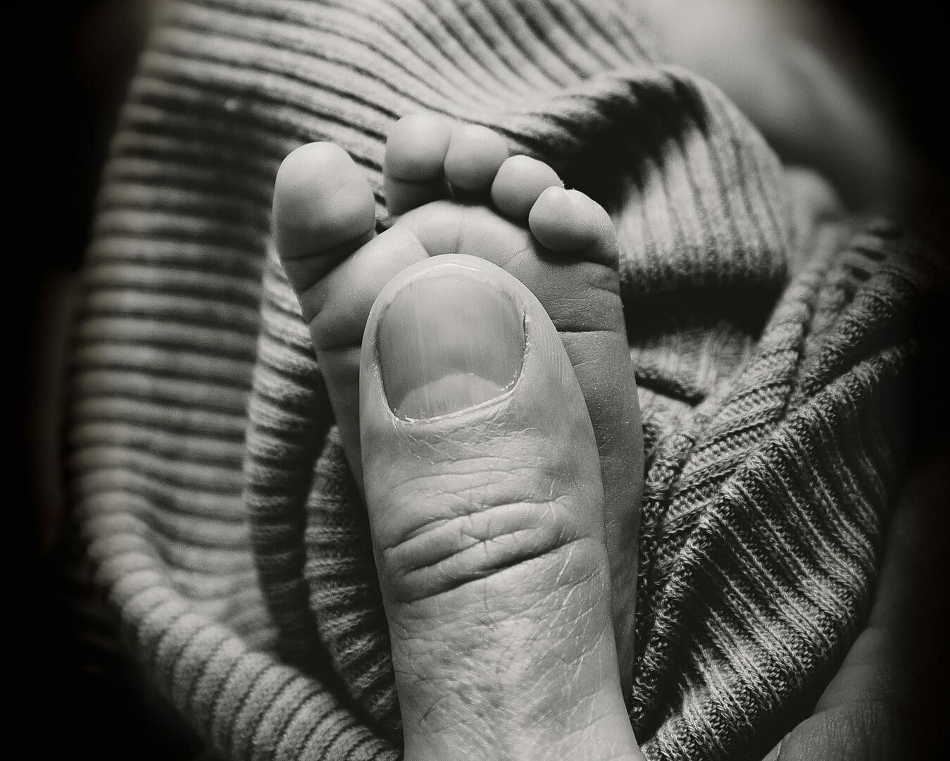 black and white photo of newborn baby toes next to the size of her daddy thumbs