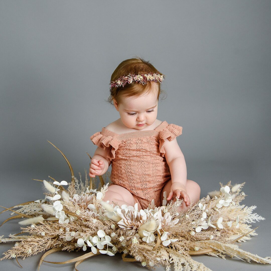 baby girl with pink romper and flowers on a grey backdrop by Older Baby photographer Mansfield, nottingham