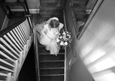 Nottingham wedding photographer - black and white photo of the bride walking down the stairs in her wedding dress.