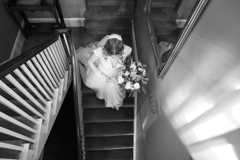 Nottingham wedding photographer - black and white photo of the bride walking down the stairs in her wedding dress.