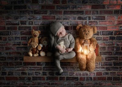 composite digital photo baby on a shelf with a brick wall behind him and some teddies sat on the shelf with him