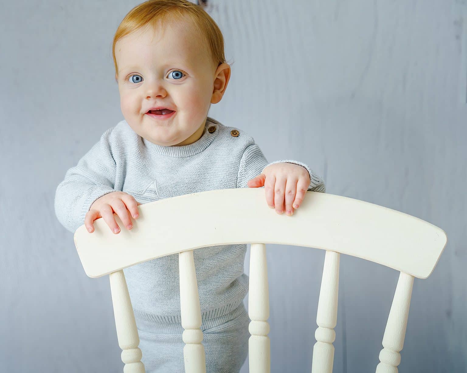 cut boy learning to stand holding a chair