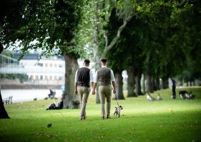 Same-Sex Couple walking their dog along the Nottingham embankment holding hands on a nice summer’s day under the tree canopy