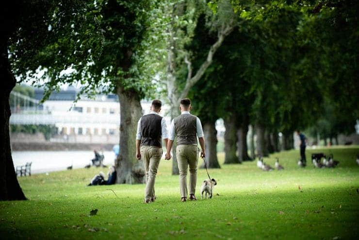 Same-Sex Couple walking their dog along the Nottingham embankment holding hands on a nice summer’s day under the tree canopy
