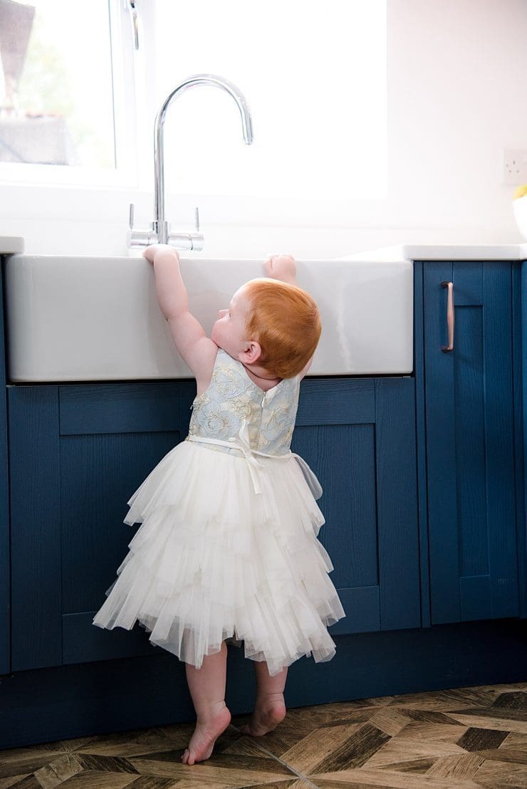 harper reaching up to the sink in a white dress