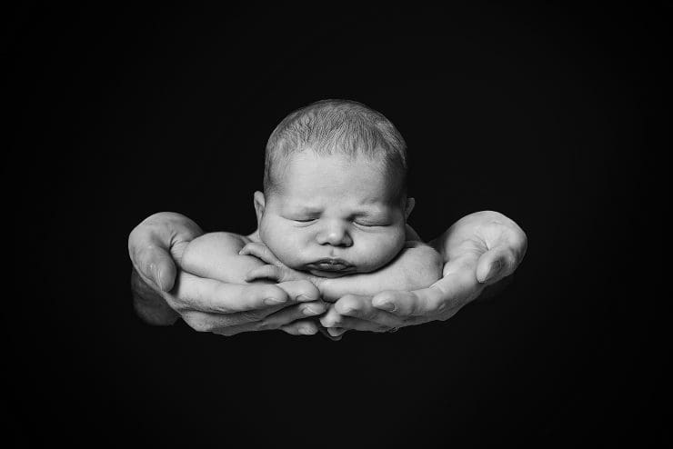 black and white photo of a newborn baby safe in daddy's hands