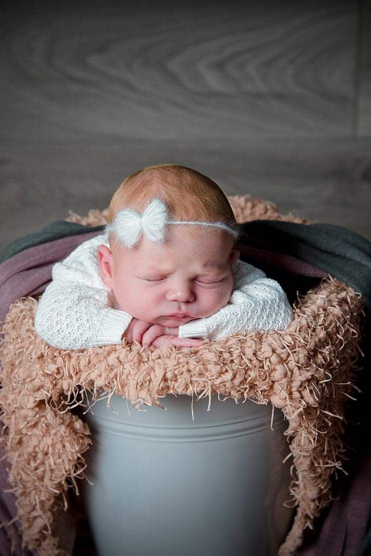 newborn baby harper in a bucket with a bow on her head