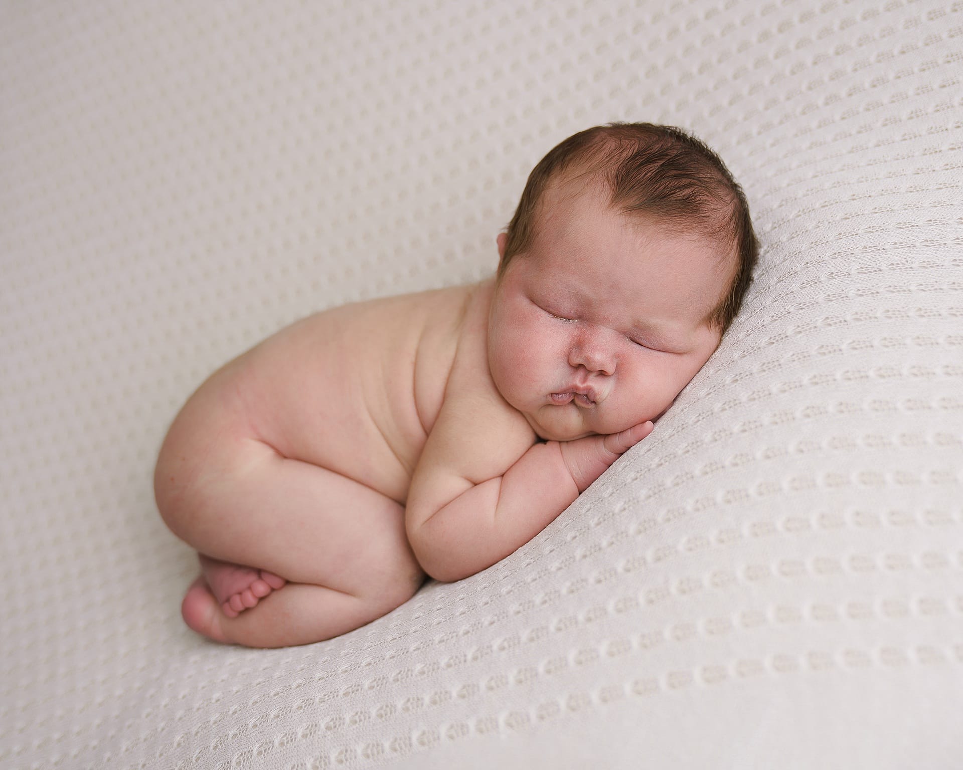 Newborn baby girl posing on his tummy on a blue blanket
