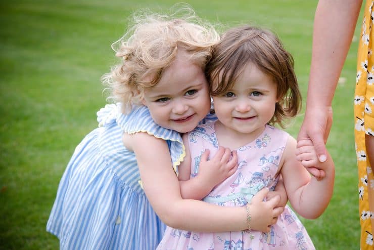two cute little girls at a wedding, one is giving the other a cuddle