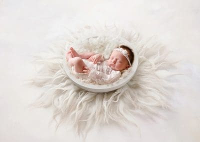little baby girl curled up in a white bowl with a fluffy white rung underneath