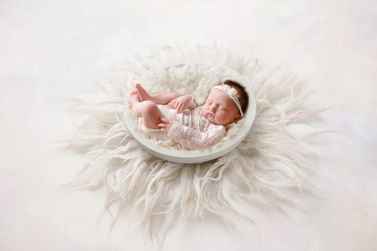 little baby girl curled up in a white bowl with a fluffy white rung underneath