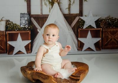 cute little boy on a plain backdrop sat in a wooden bowl
