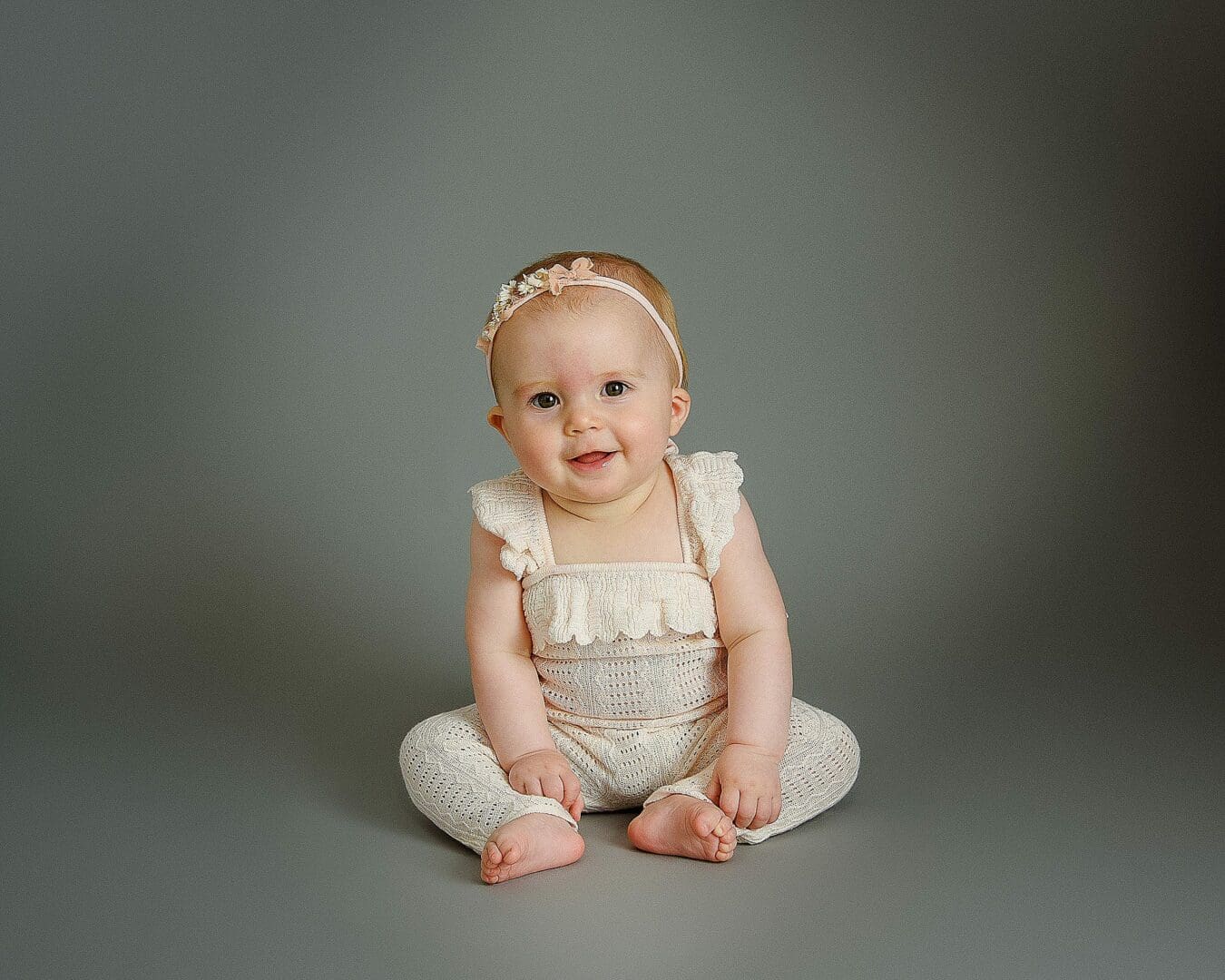 Baby girl in a white romper sitting on a grey background photographed by Older Baby photographer Mansfield, nottingham
