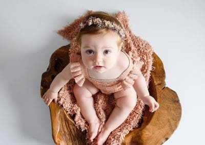 cute little girl on a plain backdrop sat in a wooden bowl
