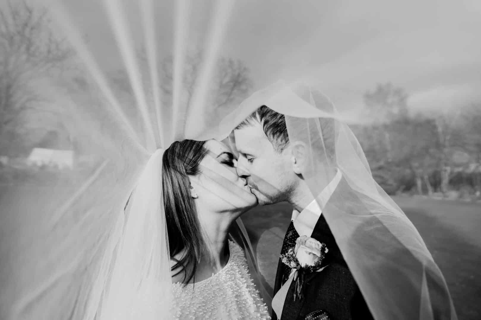 Bride and groom kissing under her veil, the photo is in black and white and its outside Cockliffe country house in Nottingham
