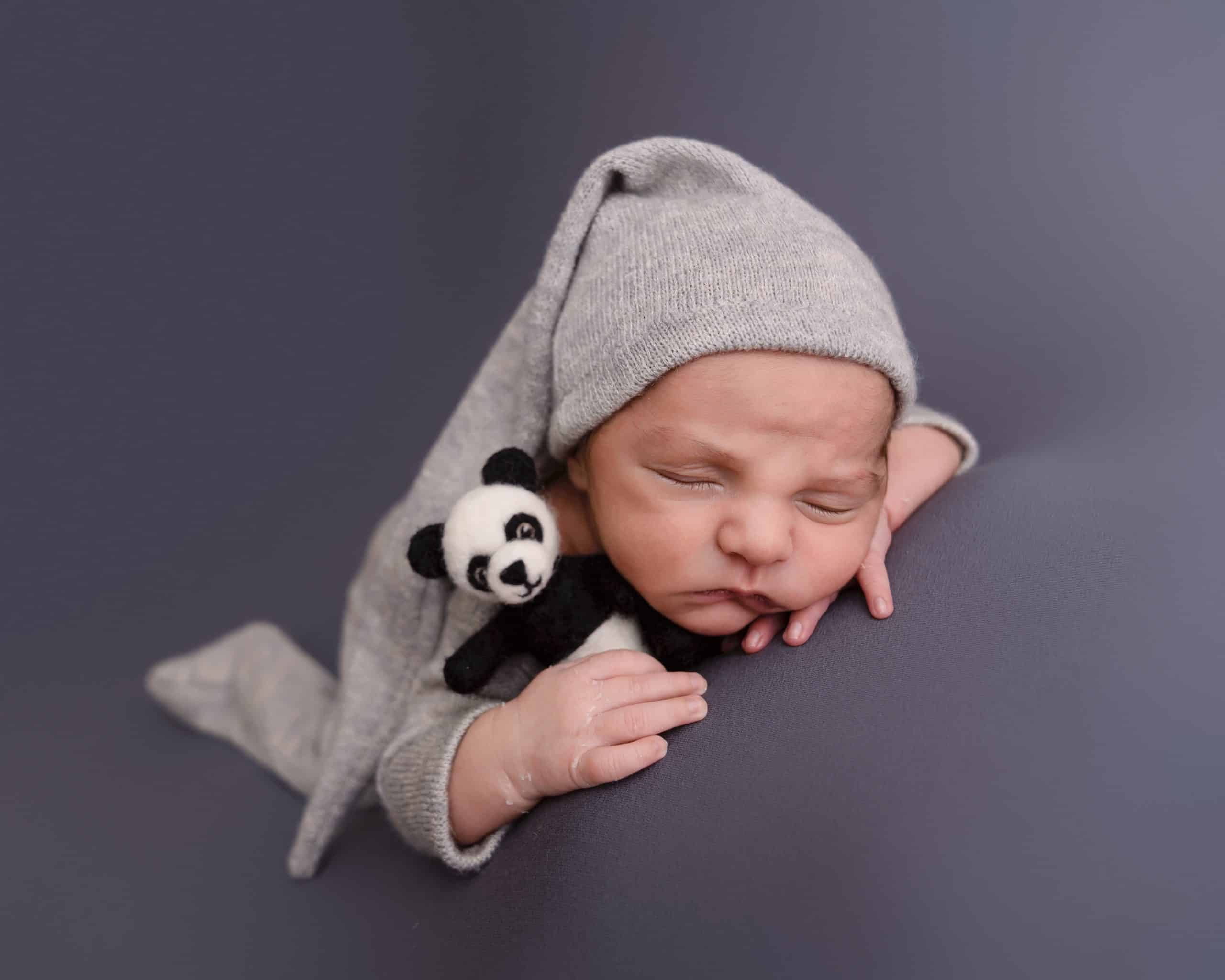Newborn baby boy laying on his front holding a panda to, he is on a grey backdrop fast asleep during his newborn session in Mansfield, Nottingham.