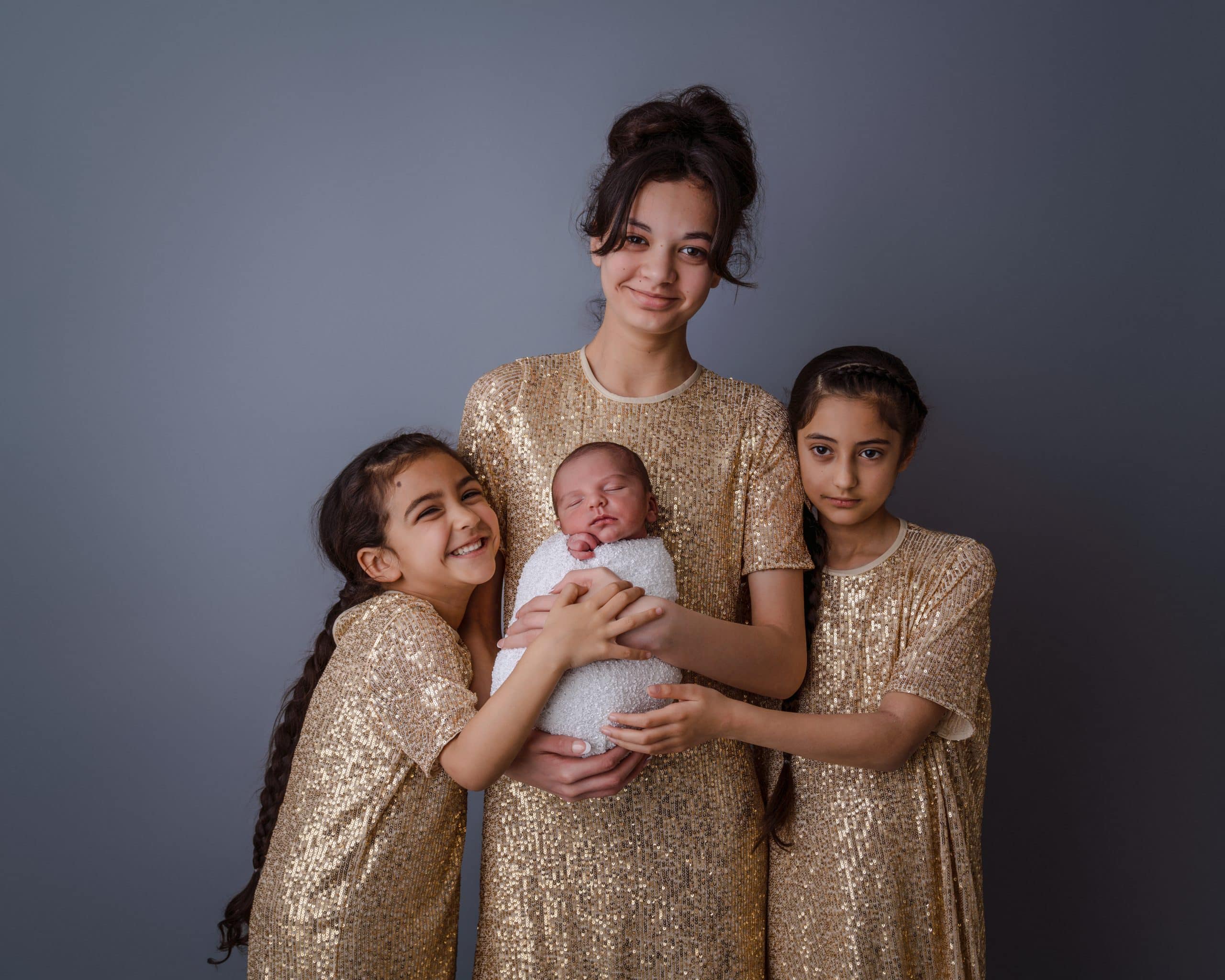 a beautiful photo of 3 sisters wearing gold with their newborn baby brother at Rachael Phillips Photography in Mansfield, Nottingham