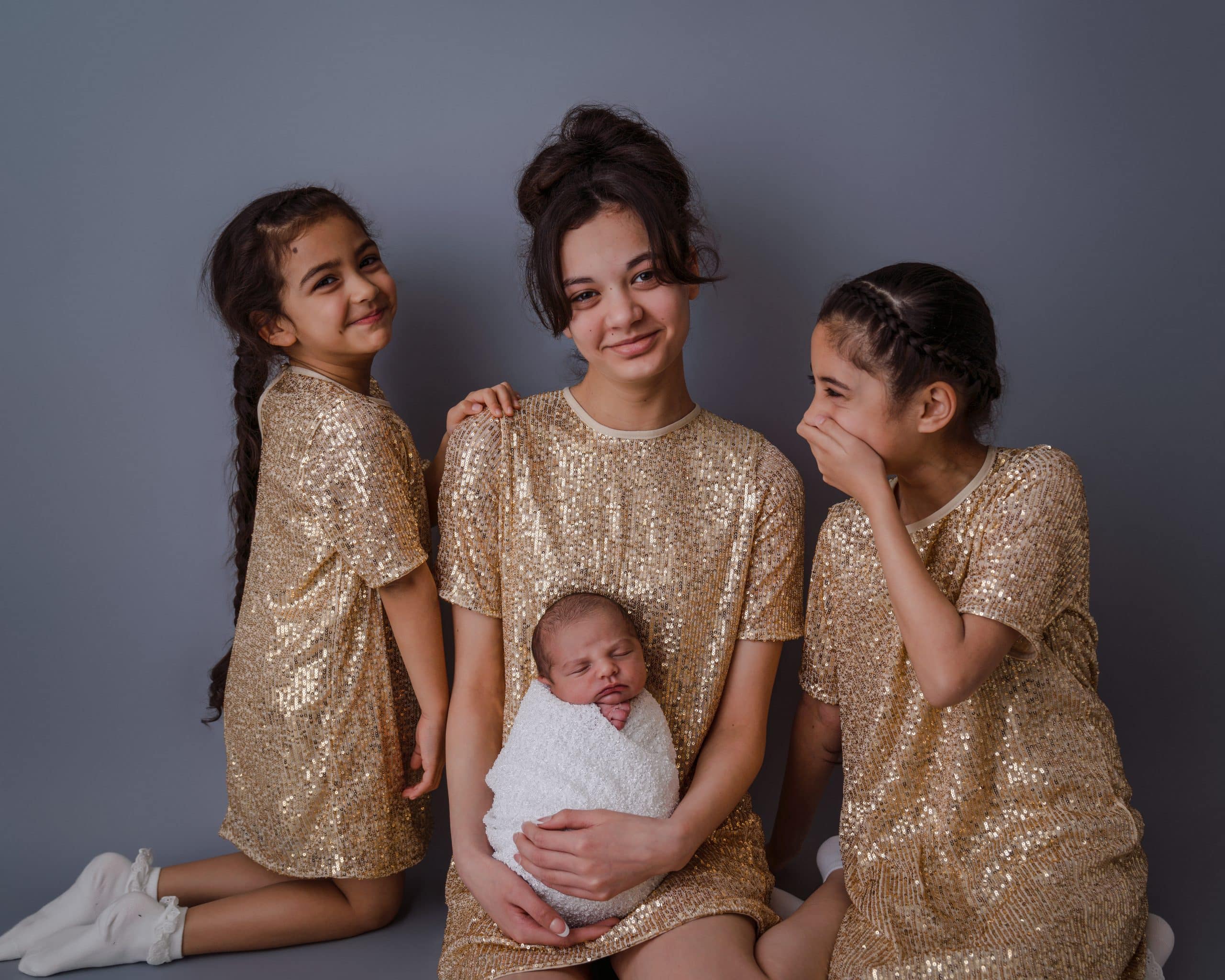 3 lovely sisters with there brother during a newborn photo session in Mansfield, one of the girls are laughing