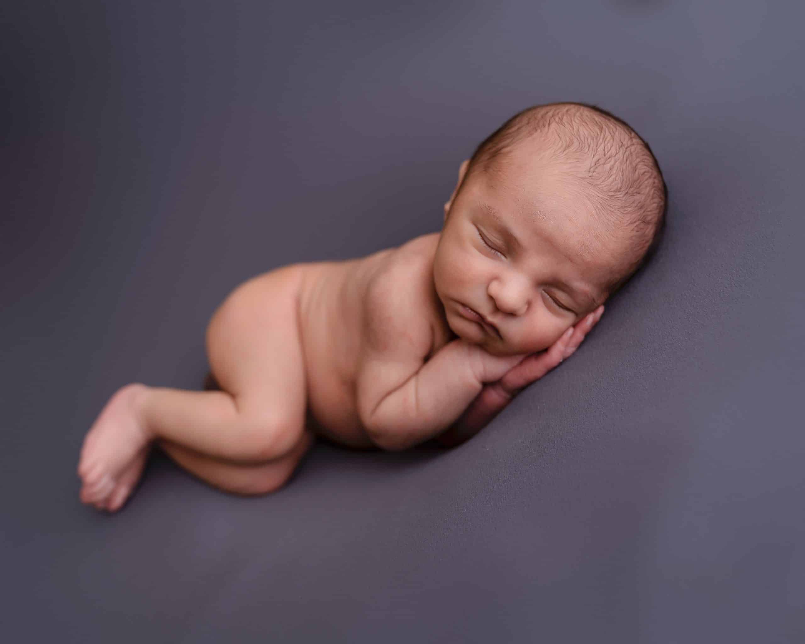 Newborn baby boy laying on his side on a grey backdrop fast asleep during his newborn session in Mansfield, Nottingham.