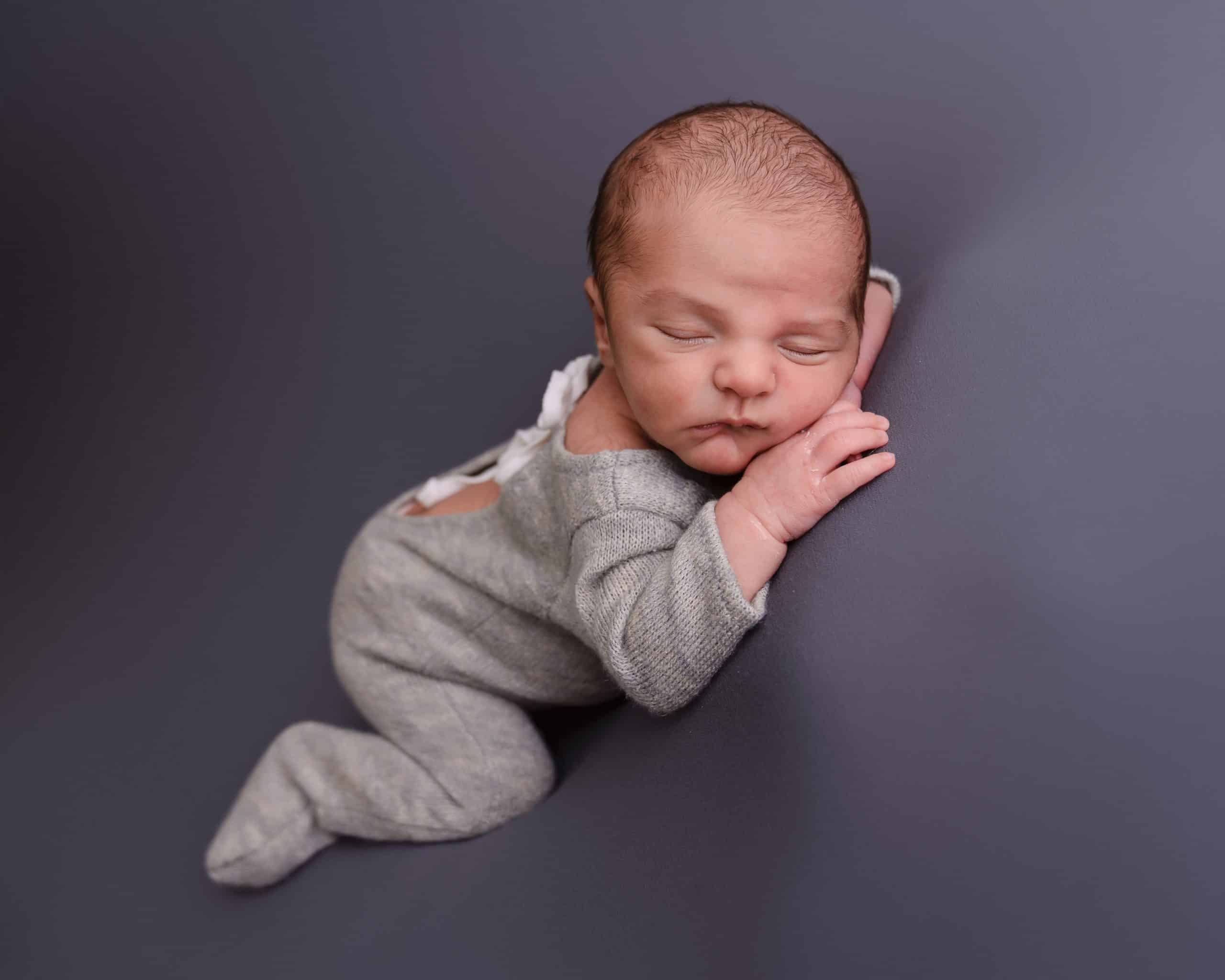 Newborn baby boy laying on his front on a grey backdrop fast asleep during his newborn session in Mansfield, Nottingham.