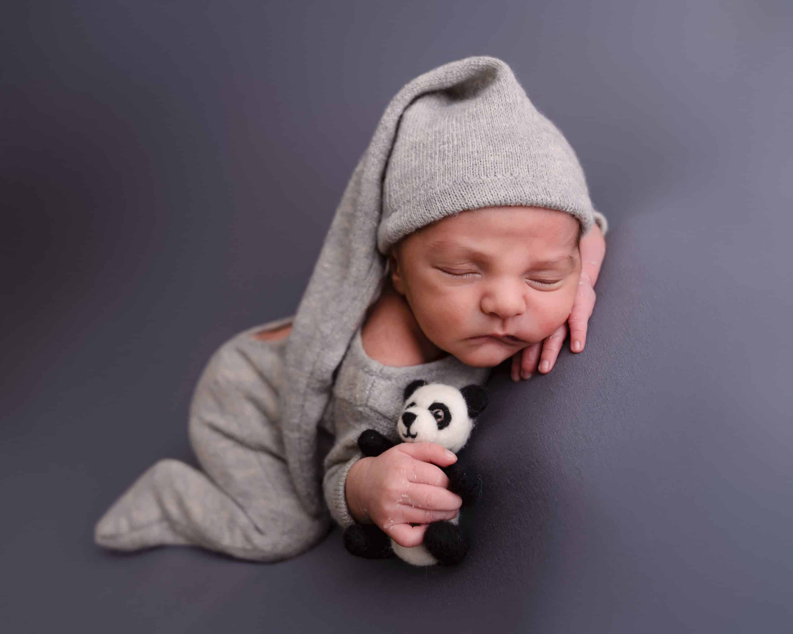 Newborn baby boy laying on his front holding a panda to, he is on a grey backdrop fast asleep during his newborn session in Mansfield, Nottingham.