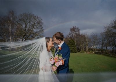 Bride and groom kissing with a swooping veil on their wedding day with a rainbow faintly behind them at Cockliffe country house in Nottingham.