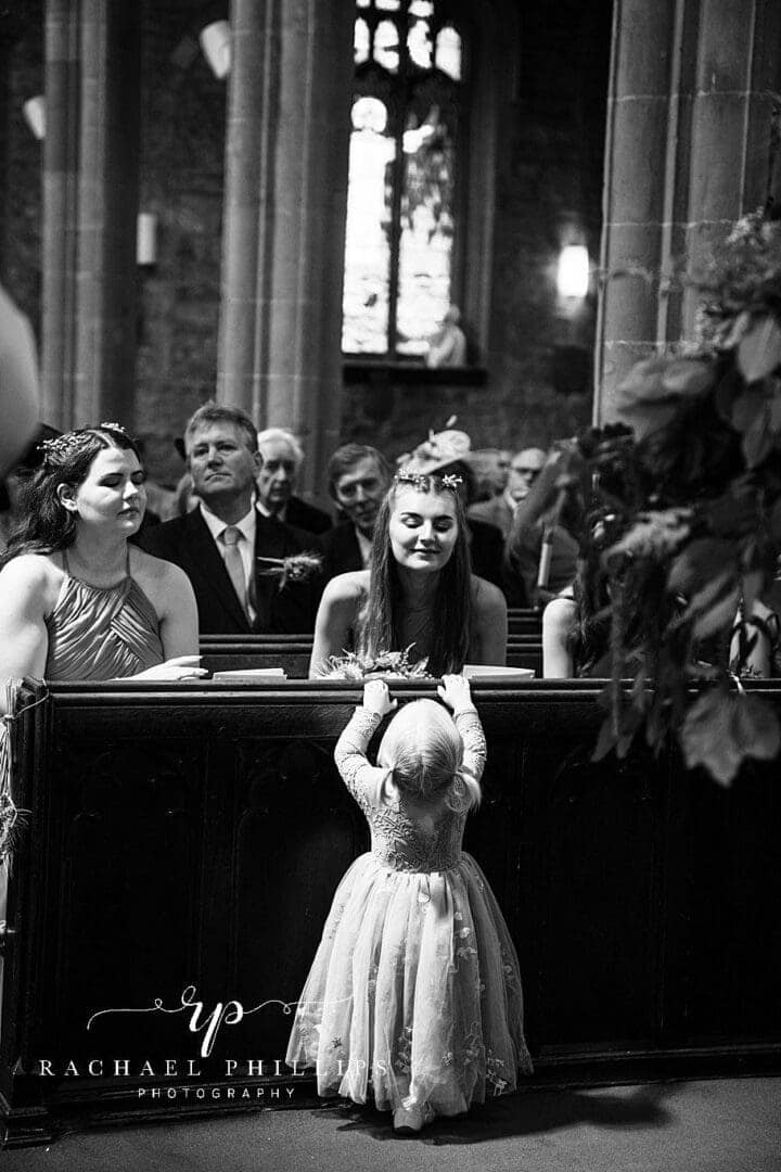 lovely black and white photo of the flower girl reaching up to see the bridesmaid in the church.