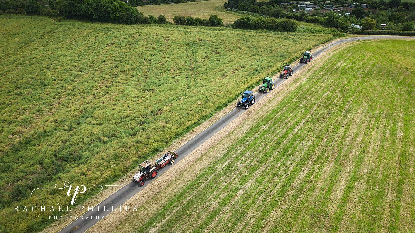 a drone photo of a convoy of tractors who are following the bride and groom who are in the main tractor