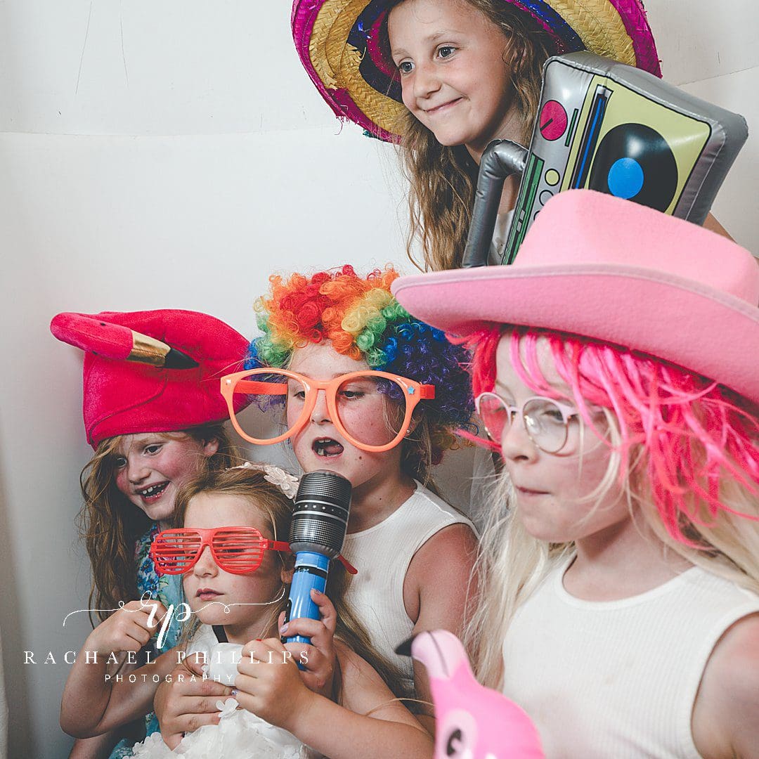 young children having fun with the Photo Booth. wearing wigs, big glasses and holding microphones