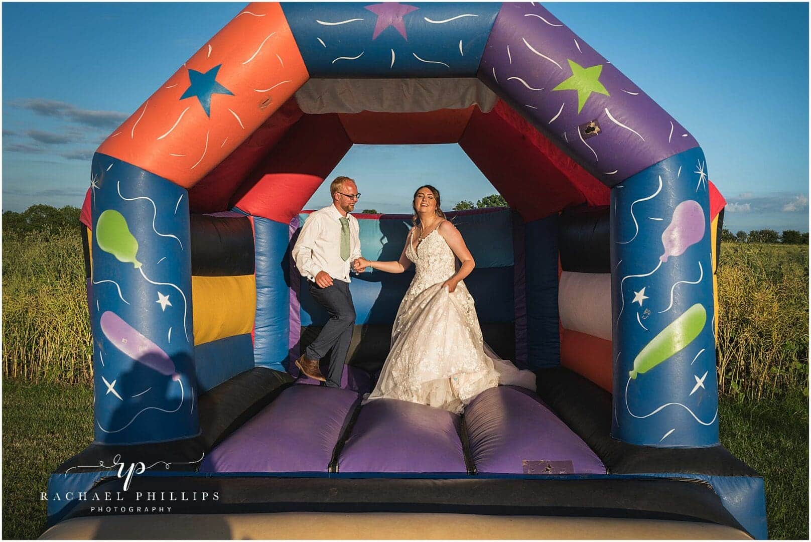 bride and groom having fun on a bouncy castle on their wedding day