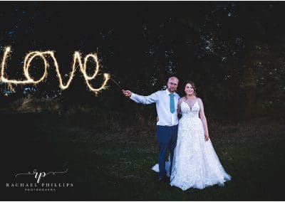 bride and groom standing nice and close while looking happy as they write the word love with sparklers on their wedding day