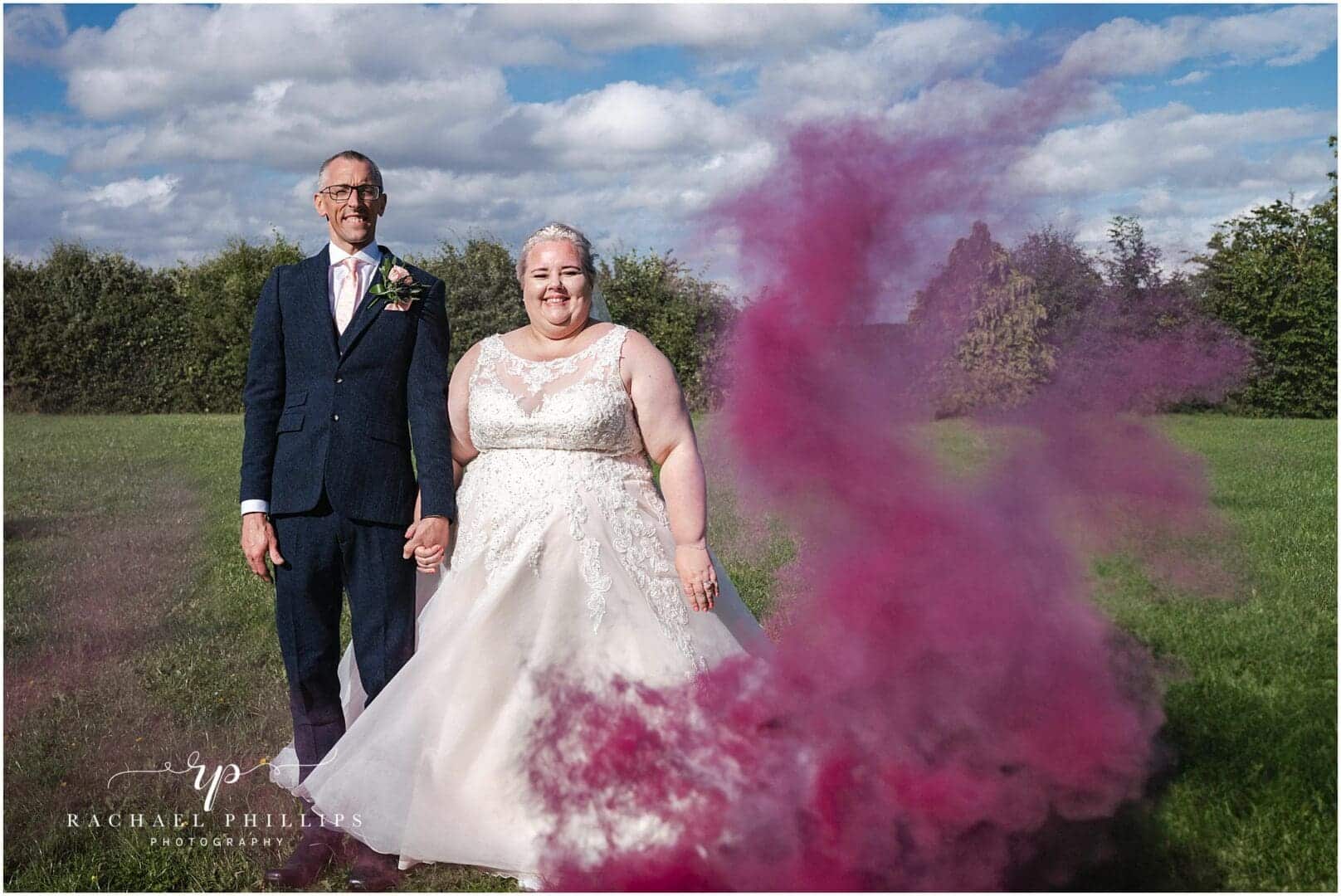 bride and groom holding hands with pink smoke around them