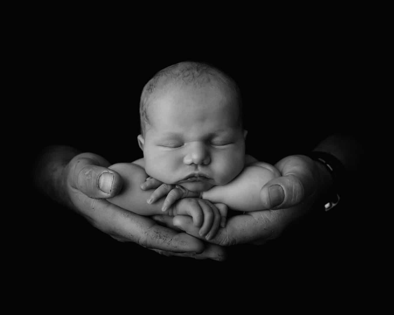 a beautiful black and white photo of a baby safe in daddy's hands