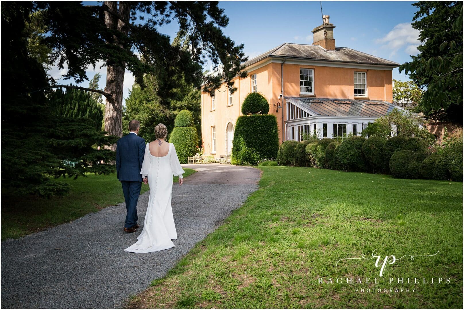 The bride and groom are walking up the drive way 
 and beautiful grounds to the front of Langar Hall in Nottingham.