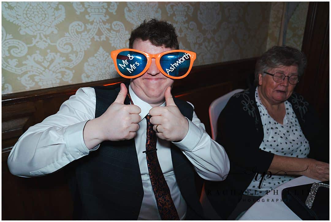 The groom is being silly wearing over sized funny glasses on the wedding day at Alfreton Hall in Derby