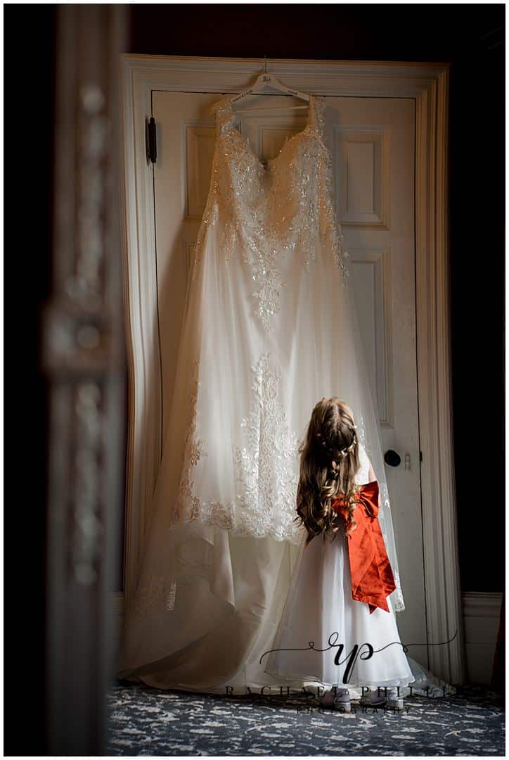 Little girl in her flower dress looking up at the brides dress