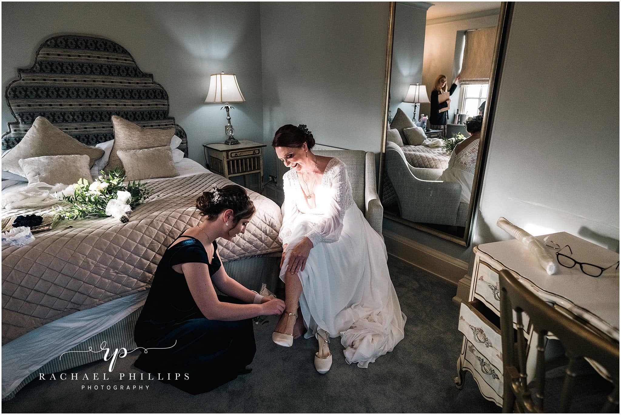 the bide is getting ready as she is helped by putting her shoes on, sat on a chair in the bridal suite at cockliffe country house in nottingham