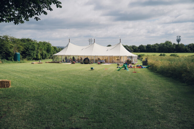 Large white marquee on grassy field under cloudy sky.
