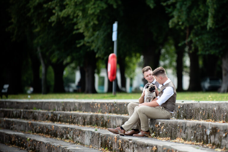 Two men sitting on steps with a pug.