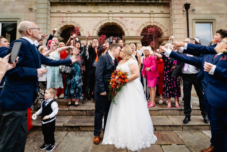 Bride and groom kiss surrounded by cheering guests.