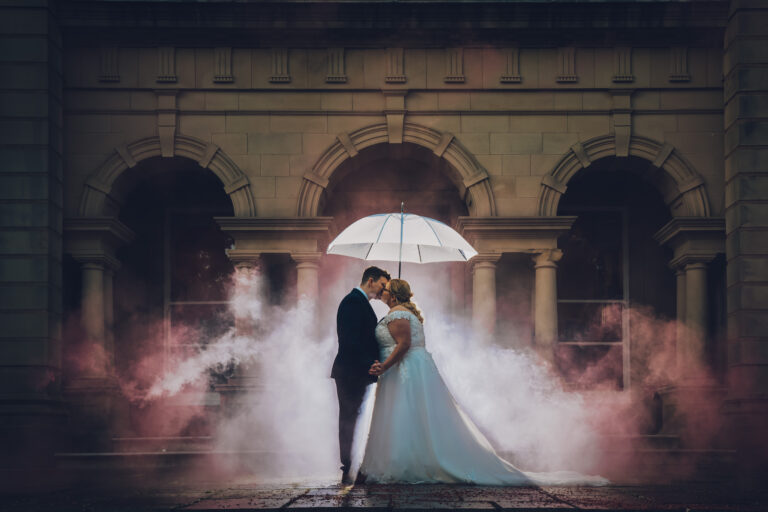 Couple kissing under umbrella outside, surrounded by smoke.