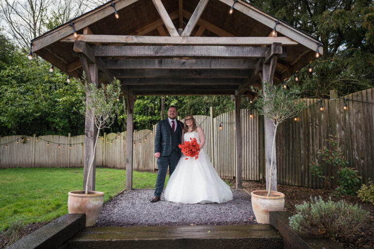 Couple under wooden gazebo at a wedding.