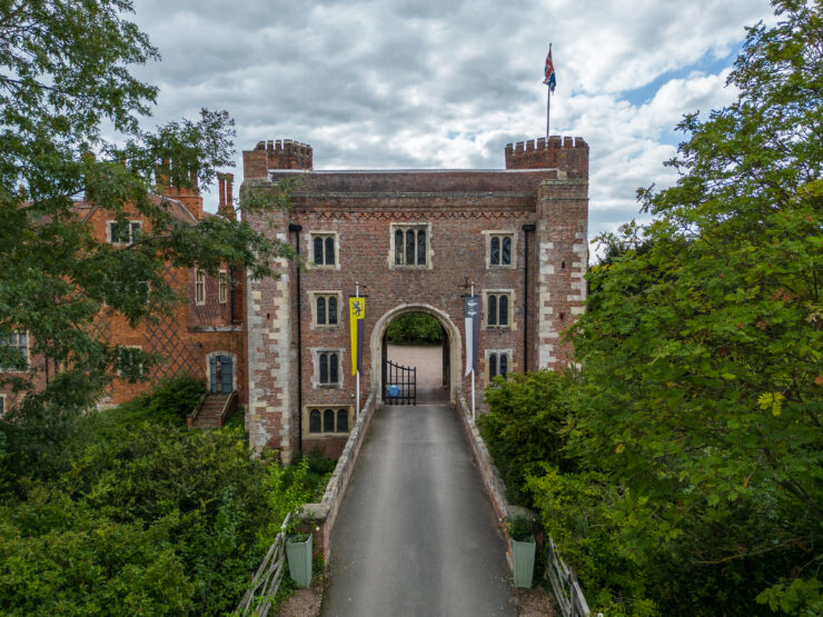Historic brick gatehouse with flag surrounded by greenery.