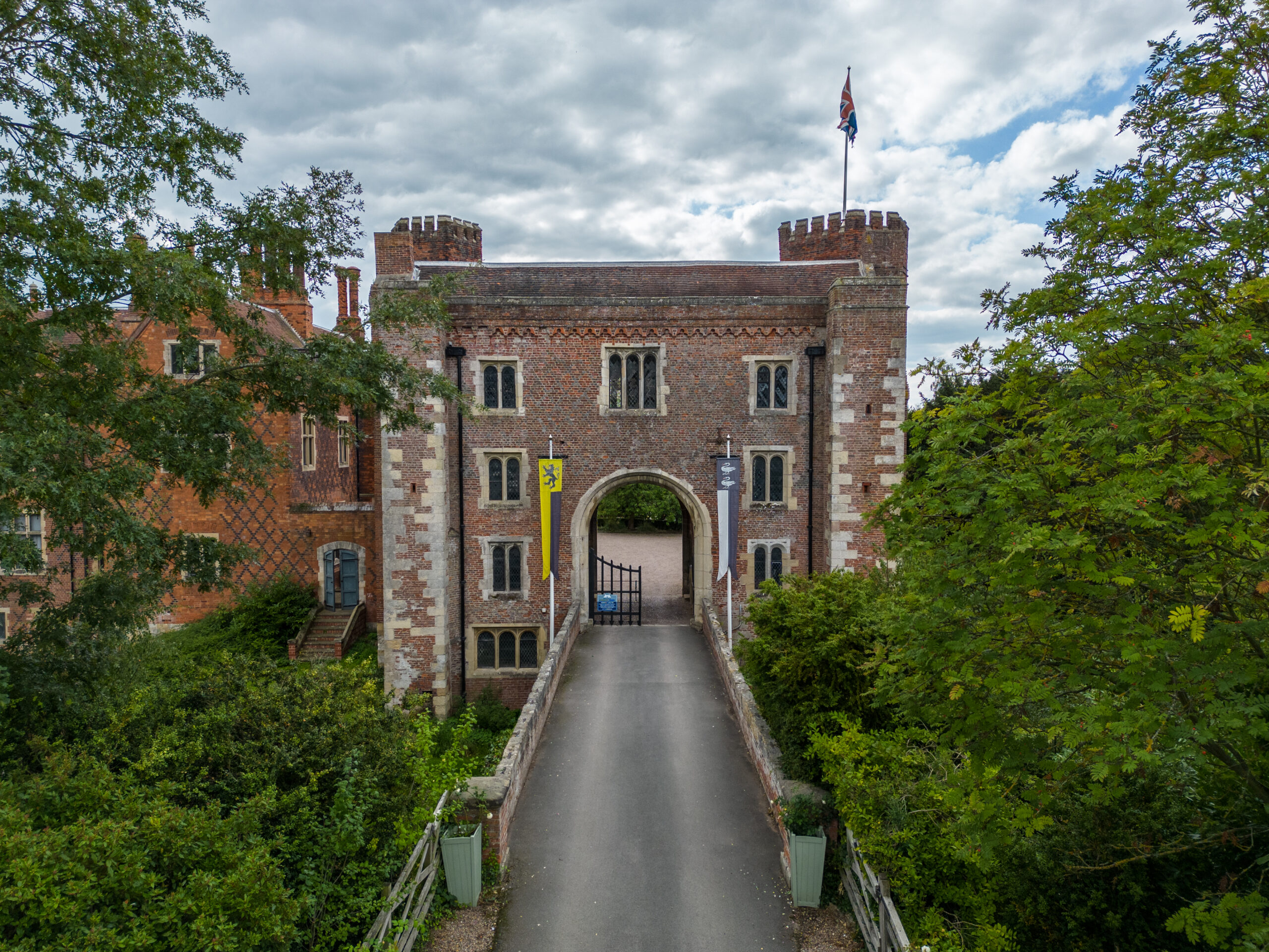 Historic brick gatehouse with flag surrounded by greenery.