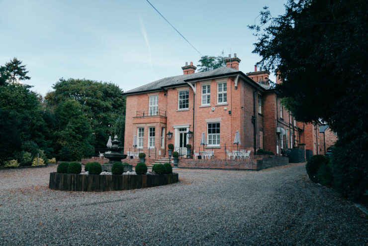 Large brick house with gravel driveway and trees.