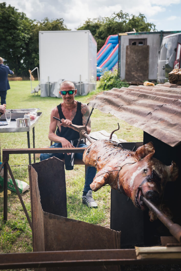 Man roasting pig on spit at outdoor event.